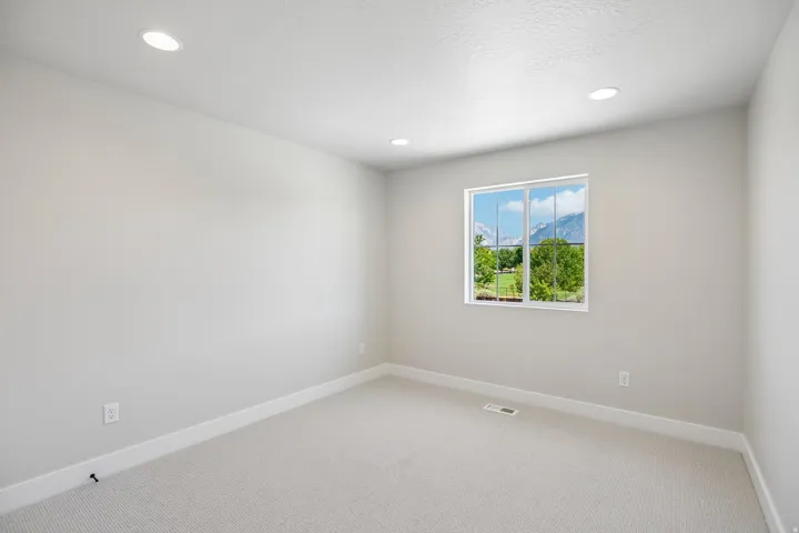 Light gray wall paint with white trim, recessed ceiling lighting, light-toned carpet, and a framed window featuring a mountain and tree landscape