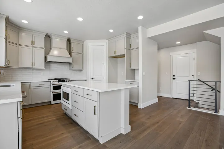 Open-concept kitchen featuring light-toned cabinetry with gold-finish hardware, a center island with integrated microwave, a built-in double oven, and wood-finish flooring