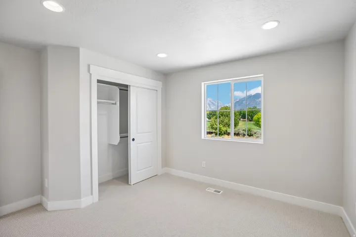 Neutral-toned room featuring a window with mountain and greenery scenery, light-colored carpeting, recessed ceiling lighting, and a sliding door closet with built-in shelving