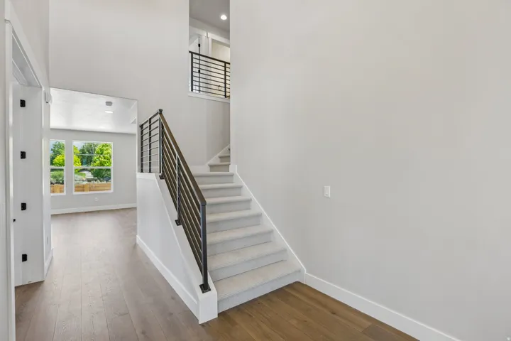 Entryway featuring wood-finish flooring, a carpeted staircase with contemporary metal railings, and a two-story ceiling