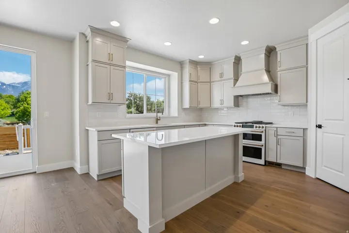 Modern kitchen featuring a central island with a solid surface countertop, light gray cabinetry, white subway tile backsplash, stainless steel range with double oven, and wood-finish flooring