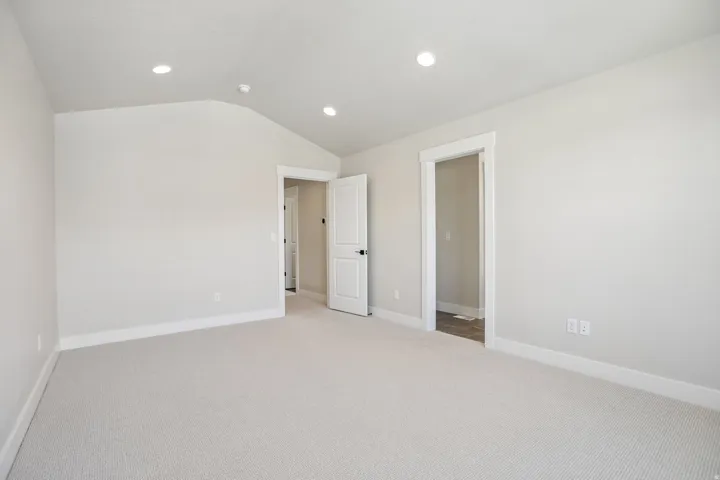 Spacious room featuring vaulted ceilings, recessed lighting, neutral wall tones, light-toned carpeting, and crisp white trim