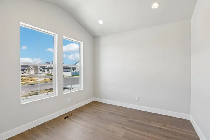 Bright interior space featuring two large windows, wood-finish flooring, recessed lighting, and a vaulted ceiling
