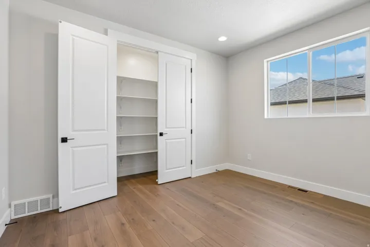 Room featuring wood-finish flooring, a large multi-pane window, recessed lighting, and a closet with bifold doors and built-in shelving