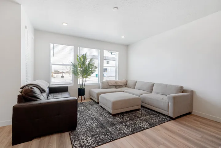 Spacious living area featuring light wood-finish flooring, recessed lighting, and multiple windows with blinds
