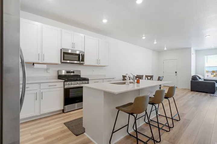 Modern kitchen featuring white cabinetry, stainless steel appliances including a gas range and microwave, and a quartz countertop island with seating for three