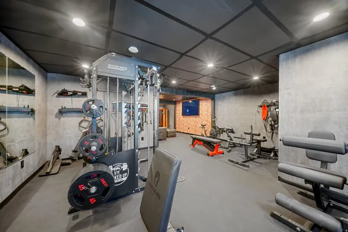 Dedicated fitness room featuring textured wall finishes, recessed lighting, and a grid-patterned ceiling