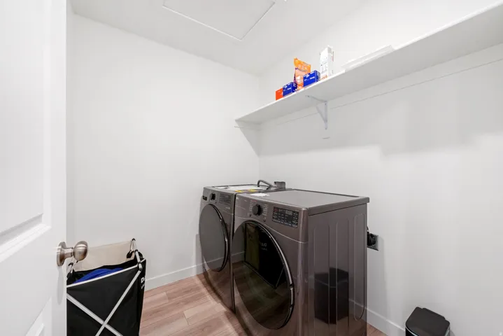 Dedicated laundry area featuring wood-finish flooring, white walls, a built-in wall shelf, and an access panel