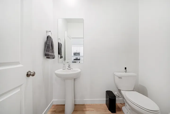 Bathroom with wood-finish flooring, a white pedestal sink, and a white toilet