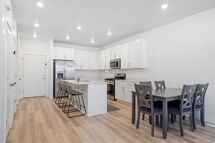 Open-concept kitchen and dining area featuring light wood-finish flooring, white cabinetry, stainless steel appliances, a center island with counter seating, and recessed lighting