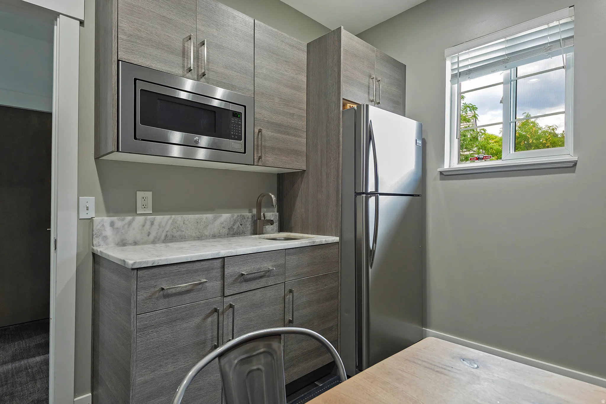 Compact kitchenette featuring wood-finish cabinetry, stainless steel appliances, and a light-toned countertop with a matching backsplash