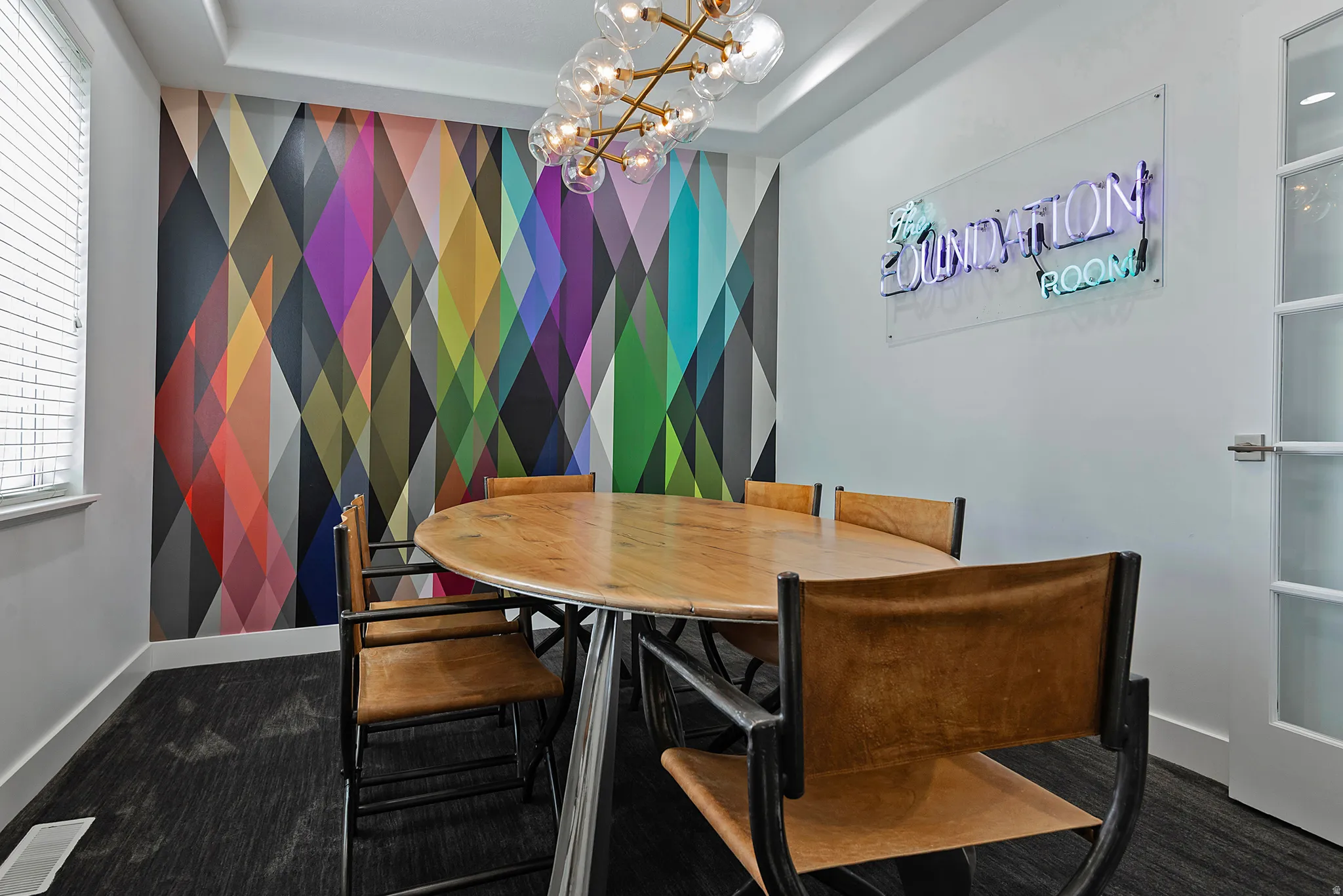 Conference room featuring a geometric accent wall, wood-finish oval table, and contemporary chandelier