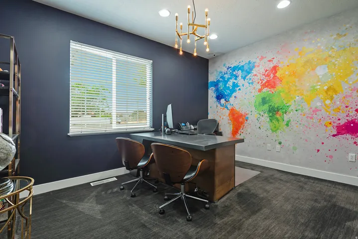 Dedicated workspace featuring a large window with blinds, a prominent accent wall with a colorful world map design, dark-toned walls, and recessed lighting