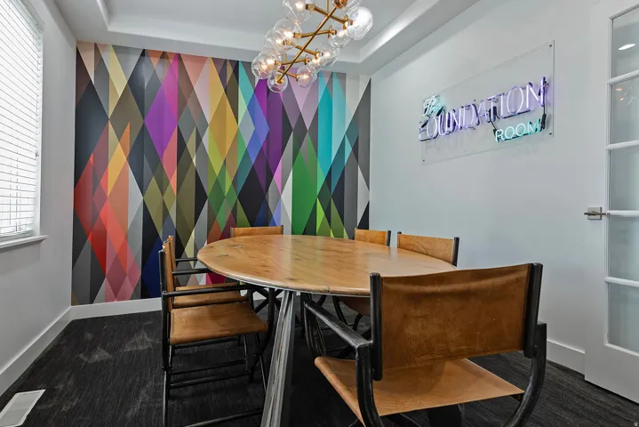 Conference room featuring a geometric accent wall, wood-finish oval table, and contemporary chandelier