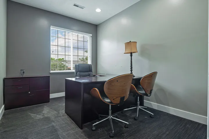 Room featuring a large window with horizontal blinds, grey textured carpeting, and white baseboards