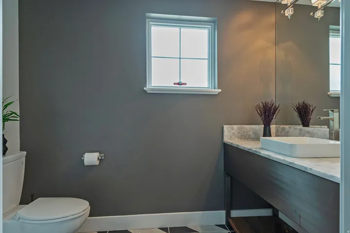 Bathroom featuring a rectangular vessel sink, stone countertop, wood-finish vanity, and a window with trim