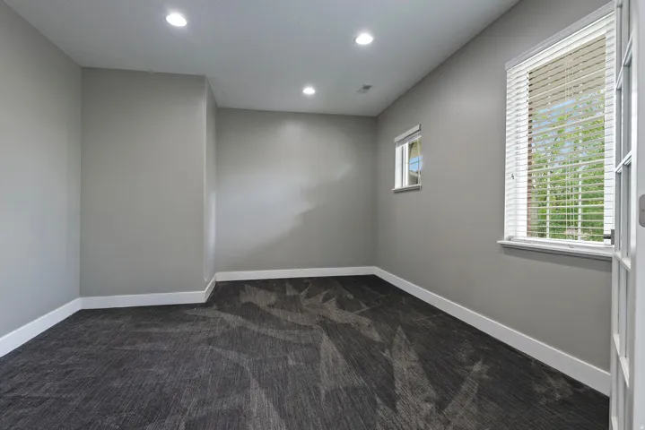 Spacious room featuring gray walls, recessed lighting, patterned carpet, and multiple windows with white blinds