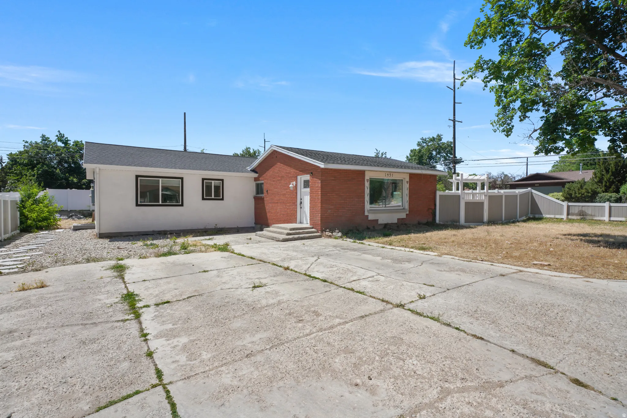 Brick exterior with white trim, featuring a concrete driveway and an additional white stucco structure with dark-framed windows