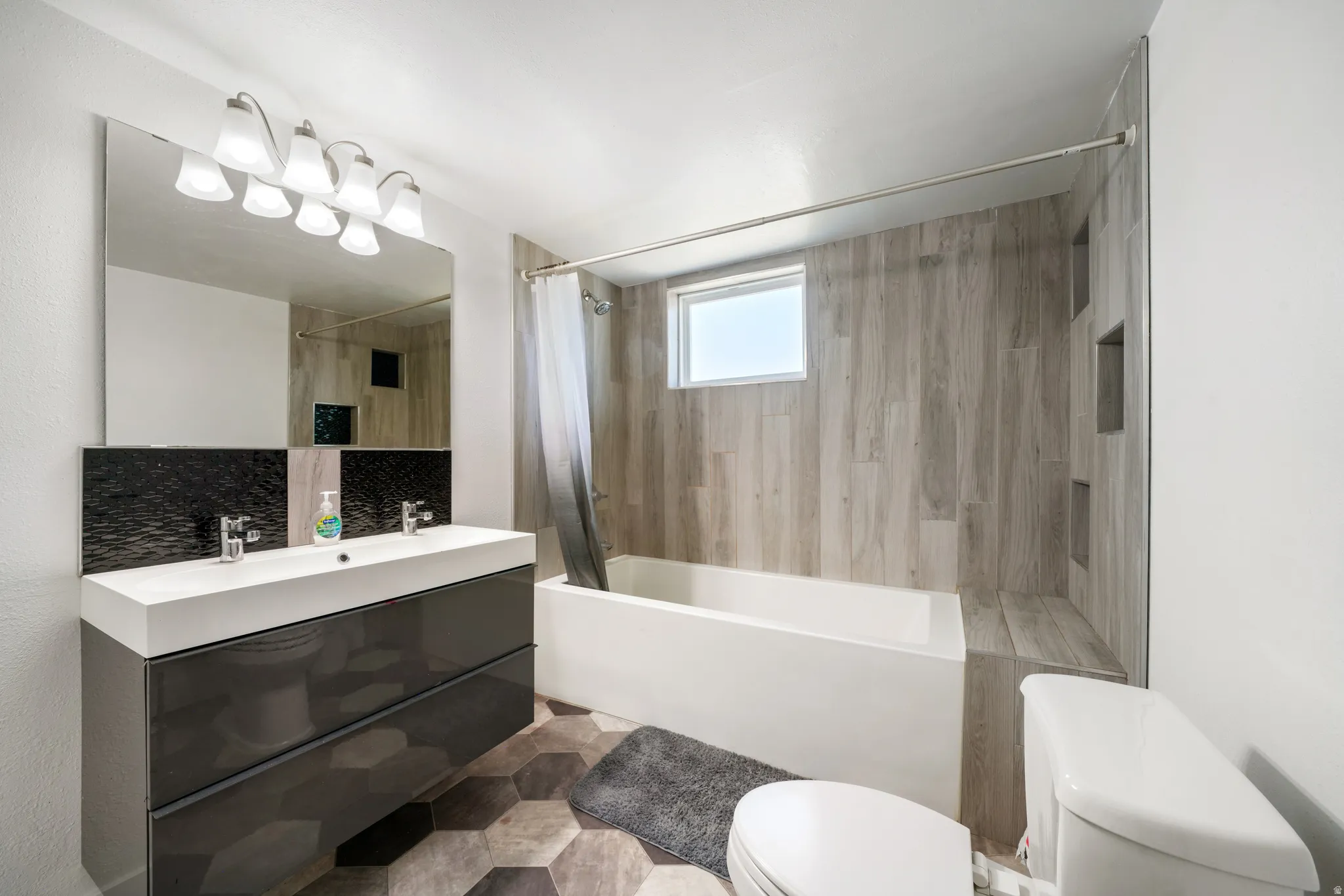 Modern bathroom featuring a dual-sink vanity with dark cabinetry, a large mirror, and a five-light fixture