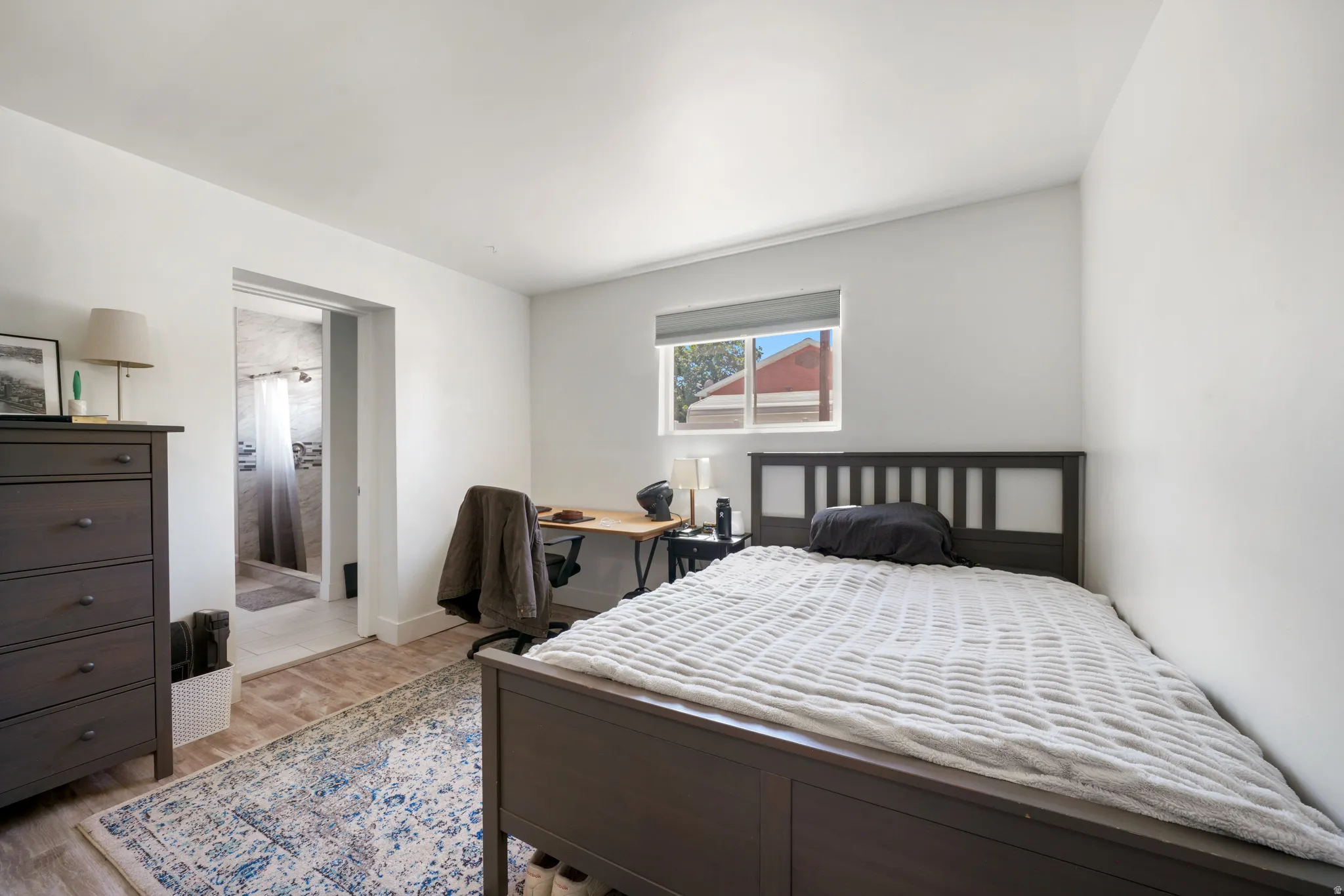 Bright interior room with wood-finish flooring and a window with roller shade