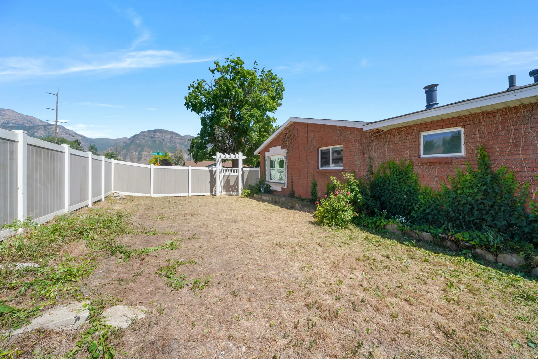 Fenced backyard featuring a white vinyl fence, a white gate with an arbor, and a brick exterior with multiple windows
