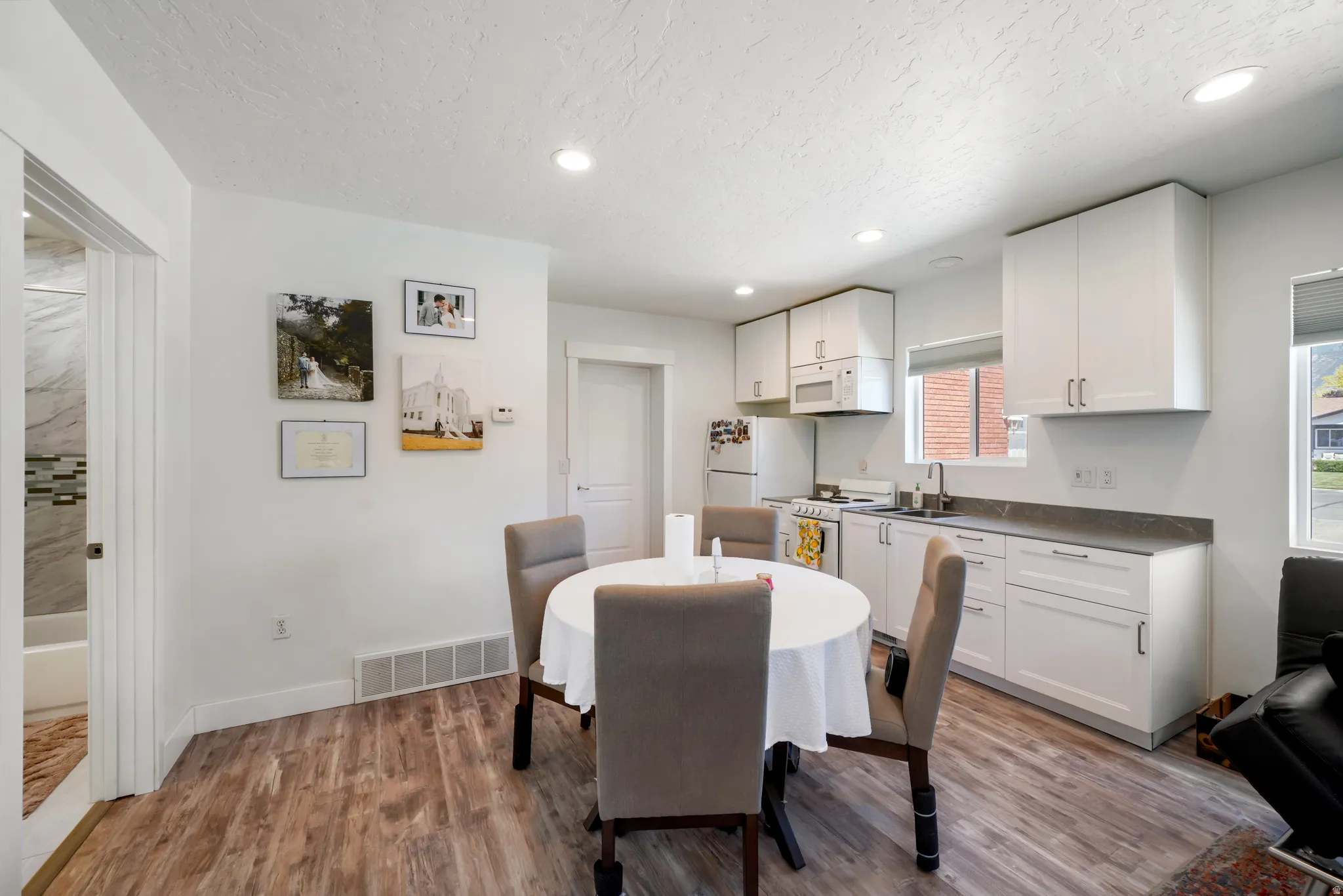 Open concept kitchen and dining area with wood-finish flooring, white cabinetry, integrated sink, and recessed lighting