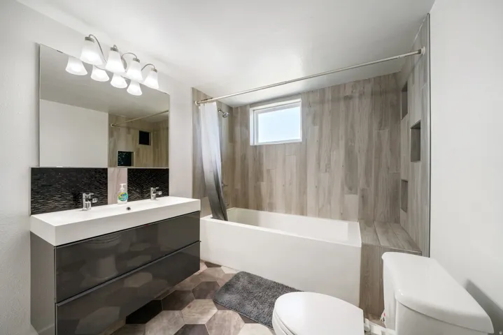 Modern bathroom featuring a dual-sink vanity with dark cabinetry, a large mirror, and a five-light fixture