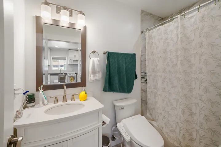 Full bathroom featuring a white vanity with an integrated sink, brushed nickel faucet, and a wall-mounted mirror with an overhead three-light fixture