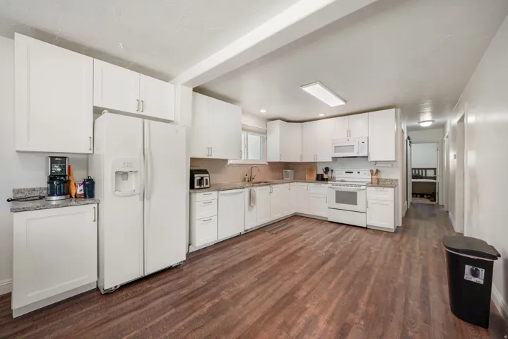 Spacious kitchen featuring extensive white cabinetry, granite-finish countertops, wood-finish flooring, and a complete suite of white appliances