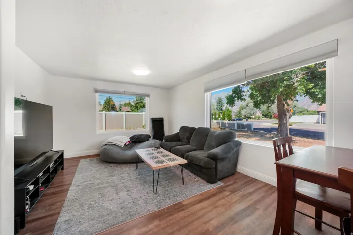 Spacious living area featuring wood-finish flooring, white walls, and a large picture window with roller shade