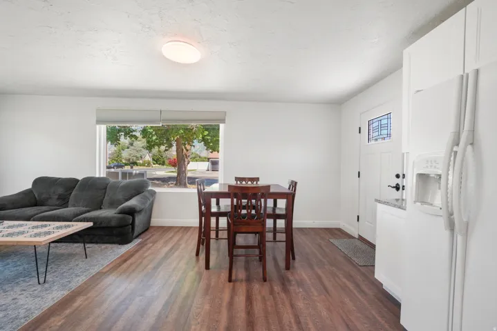 Open-concept living space featuring wood-finish flooring, white walls, and a large front-facing window with roller shades