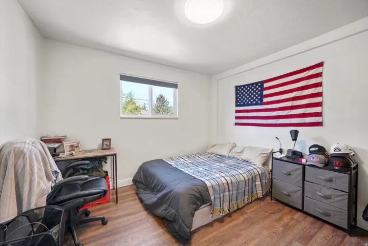 Room with wood-finish flooring, a window with roller shades, and a flush-mount ceiling light fixture