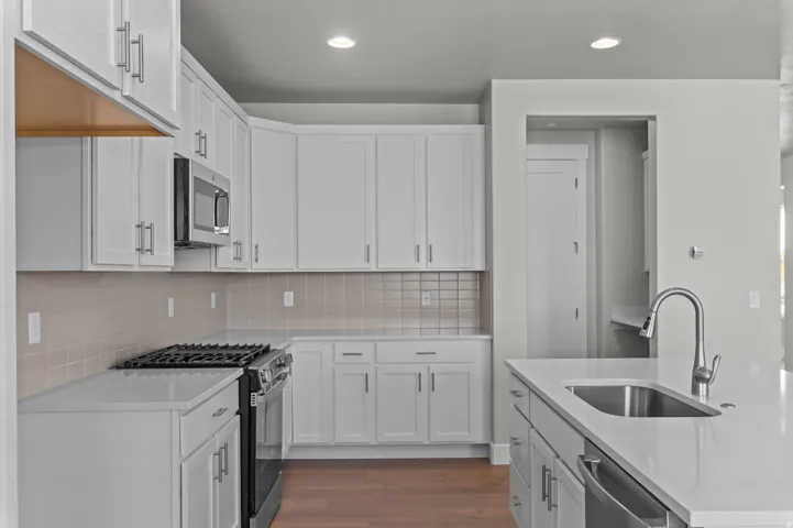 Contemporary kitchen featuring white shaker cabinetry, stainless steel appliances, a tiled backsplash, and light-toned countertops