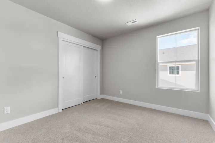 Bedroom featuring neutral-toned carpet, a double-pane window, and a sliding door closet with white trim