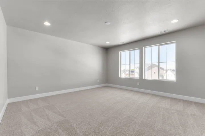Spacious room featuring two large windows, neutral gray wall paint, light-colored patterned carpeting, white baseboards, and recessed ceiling lighting