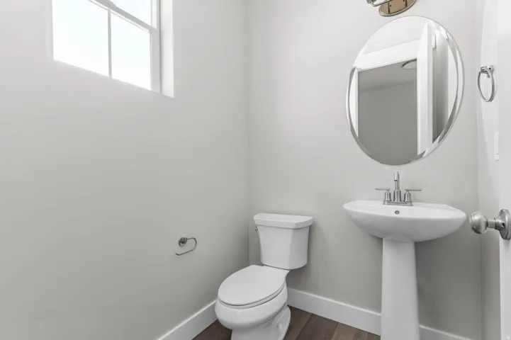 Bathroom featuring a pedestal sink, oval frameless mirror, and wood-finish flooring