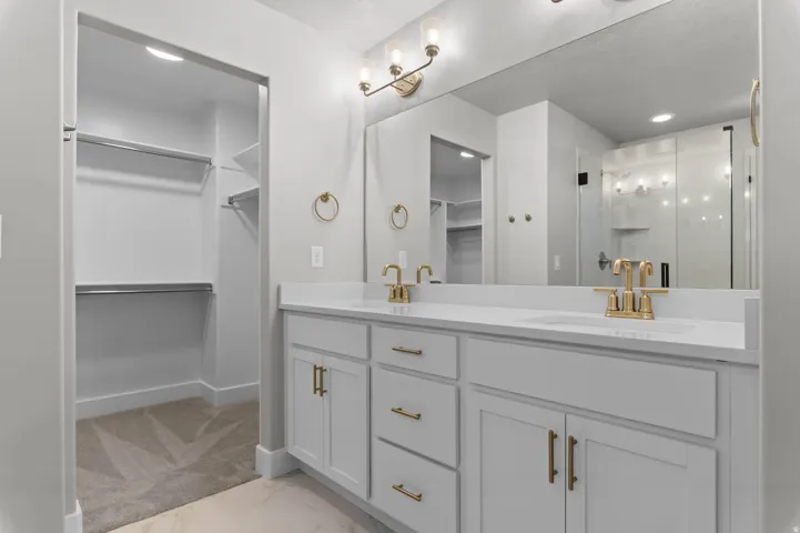 Double vanity with white cabinetry, gold-finish hardware, and a large wall-mounted mirror