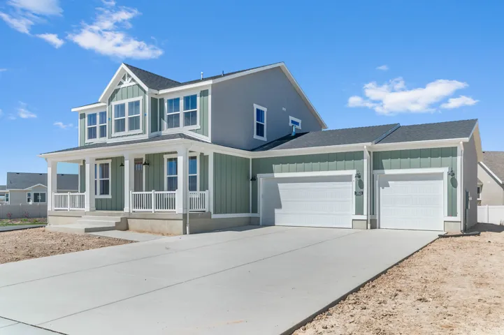 Two-story residence featuring a covered front porch with white railings, a two-car garage with separate doors, vertical and horizontal siding in contrasting tones, a dark shingled roof, and multiple windows with white trim