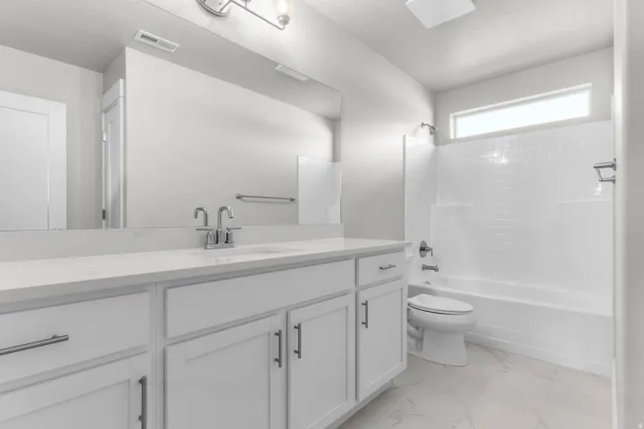 Spacious bathroom featuring a double vanity with white cabinetry and a light-toned countertop, a large mirror, and a white subway tile surround tub and shower combination with a transom window