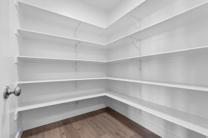 Expansive pantry featuring extensive white shelving, wood-finish flooring, and a neutral color palette