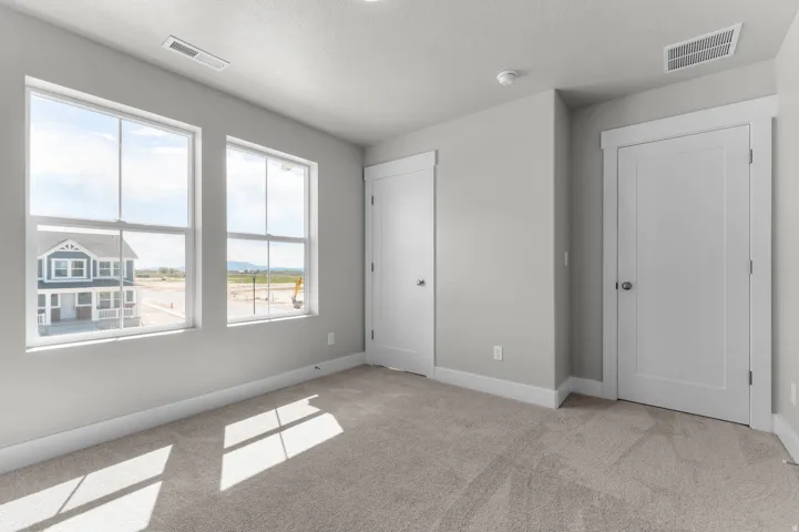 Neutral-toned carpet flooring in a bright room featuring two large windows, white trim, and two panel doors with dark hardware