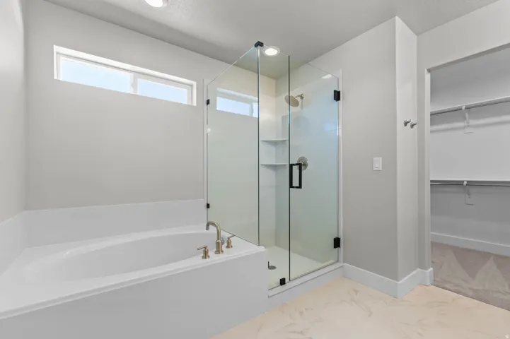 Bathroom featuring a corner soaking tub with brass fixtures, a glass-enclosed shower with black hardware, and a high horizontal window