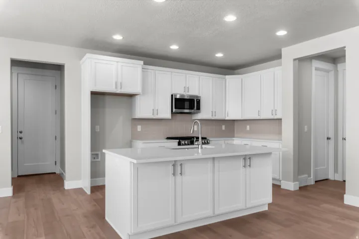 Bright kitchen featuring white shaker cabinetry, an island with integrated sink, stainless steel microwave, and wood-finish flooring