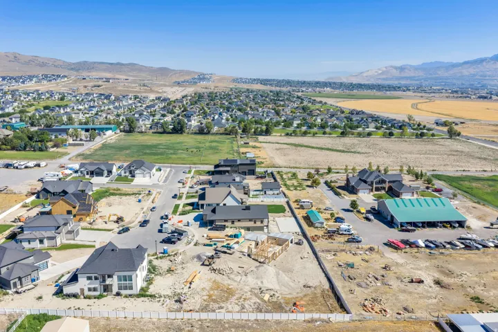 Aerial perspective displaying a developing residential neighborhood with established homes and ongoing construction, surrounded by open fields and distant mountains