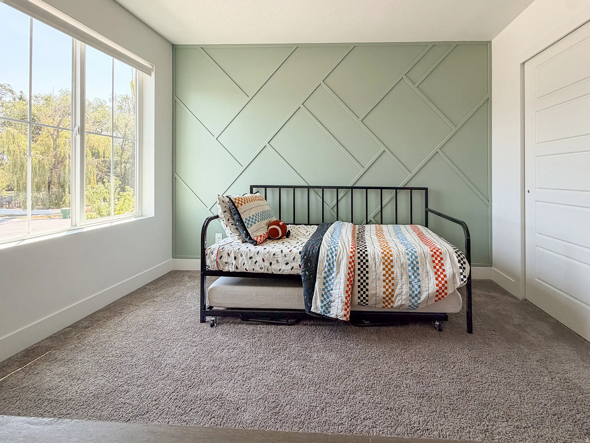 Accent wall featuring geometric panel molding, light neutral carpeting, wide window with white trim, and a white paneled door