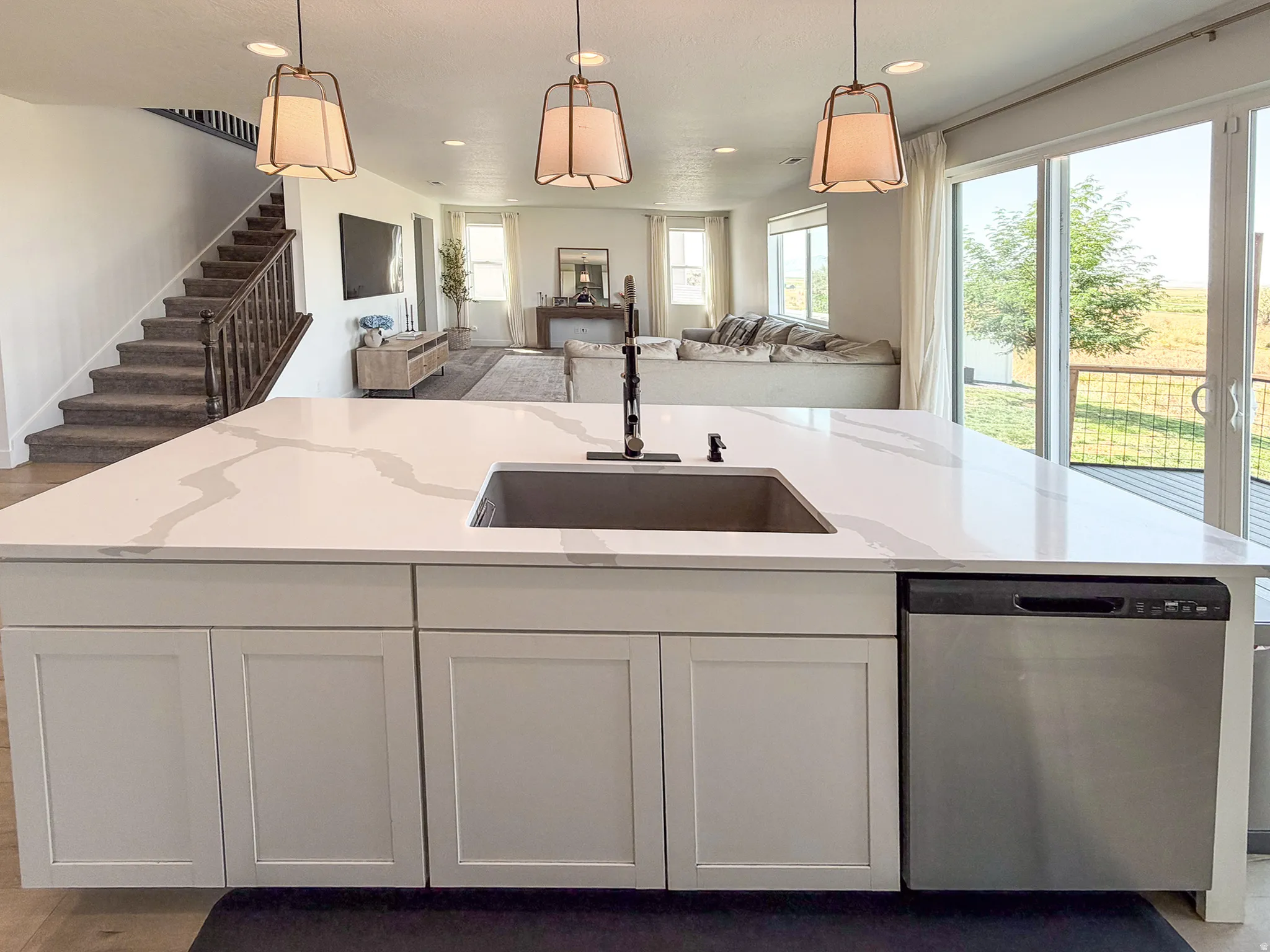 Spacious kitchen island featuring a waterfall-edge countertop, undermount sink with a matte black faucet, and integrated dishwasher