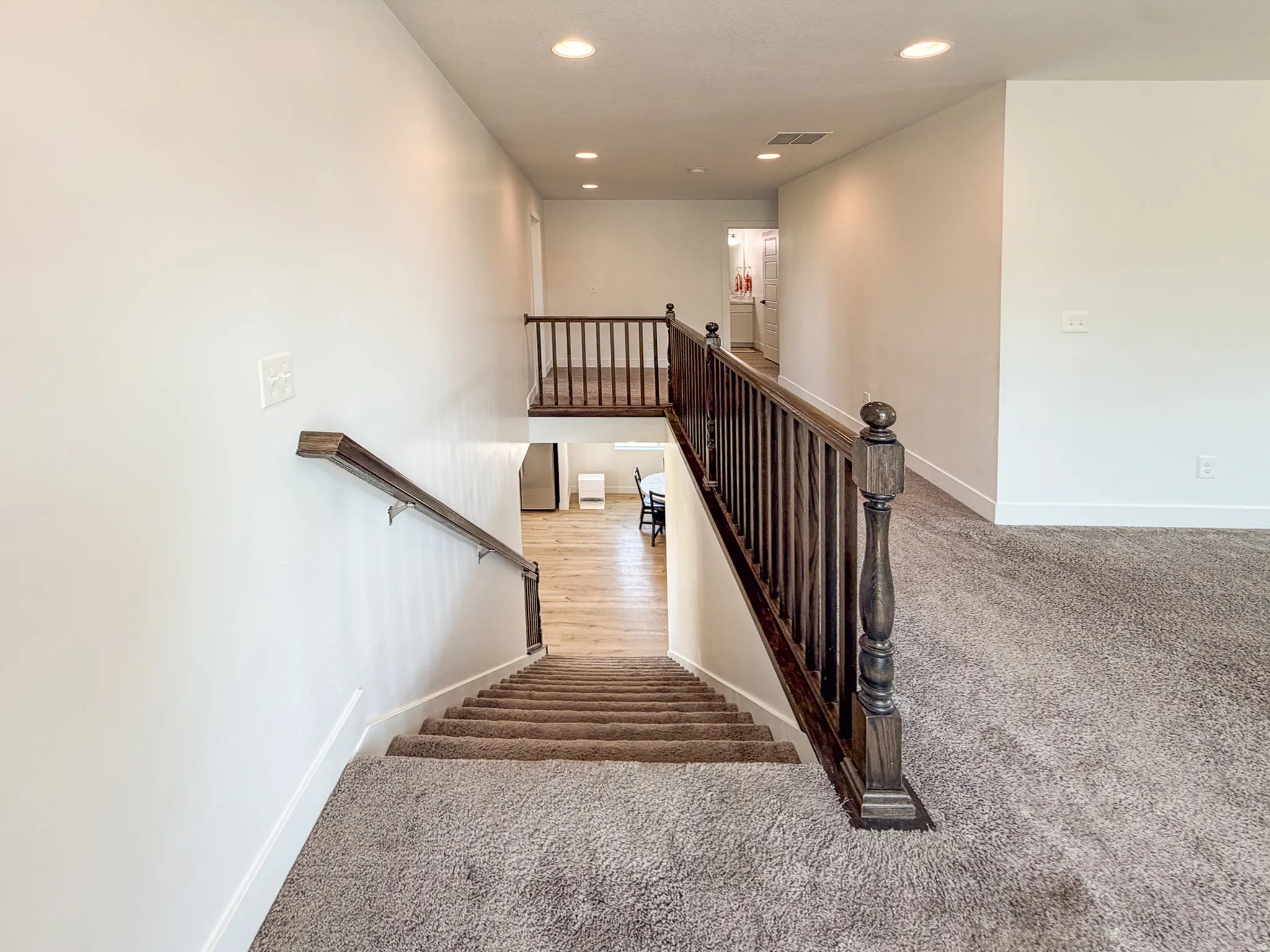 Carpeted staircase with dark wood-finish handrail and balusters, leading to a lower level featuring wood-finish flooring