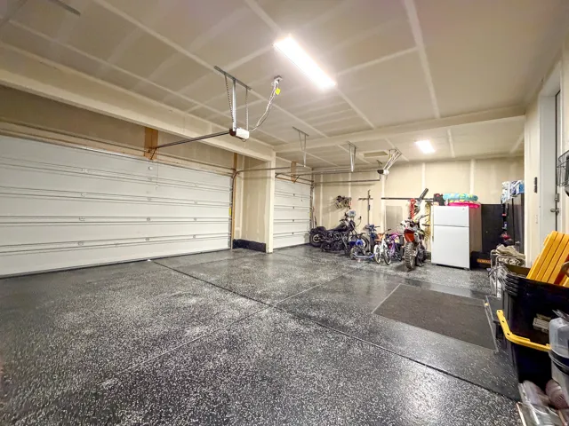 Spacious multi-car garage featuring a speckled epoxy floor coating, multiple overhead garage doors, and ample ceiling-mounted lighting