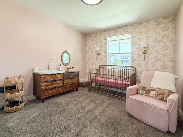 Carpeted room featuring a window with natural light, a floral accent wall, and two wall-mounted sconces