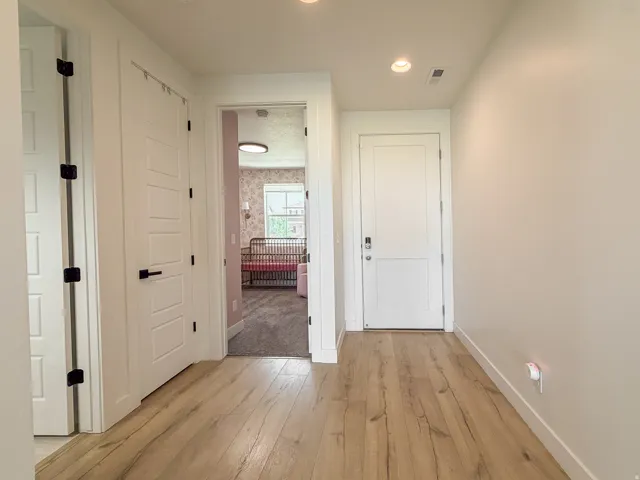 Hallway featuring wood-finish flooring, recessed lighting, and white paneled doors with matte black hardware
